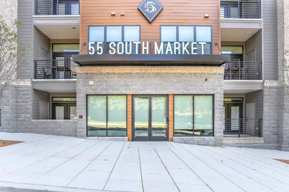 This image presents the building’s exterior facade, with clear views of the entrance doors and visible signage displaying the property name. The scene exudes a welcoming atmosphere, capturing the sense of arrival and security provided to guests. The entryway is well-lit, and the surrounding plaza hints at the building’s modern amenities and community feel.