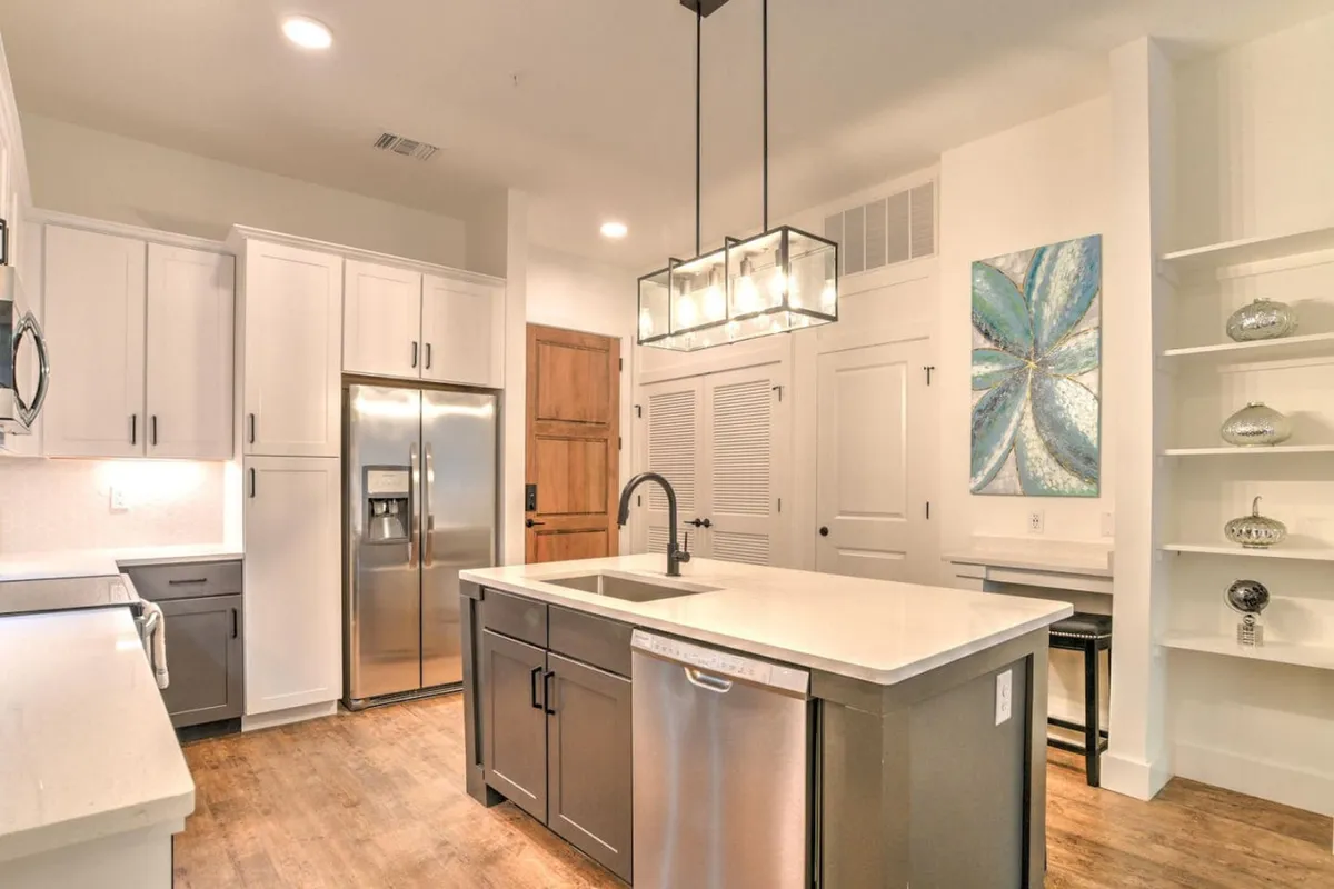 A contemporary kitchen scene with a stylish island countertop, pendant lighting, stainless steel appliances, and decorative wall art. The generous workspace and modern touches create an environment equally suited to quick breakfasts or family gatherings, reinforcing the kitchen's central role in daily life.
