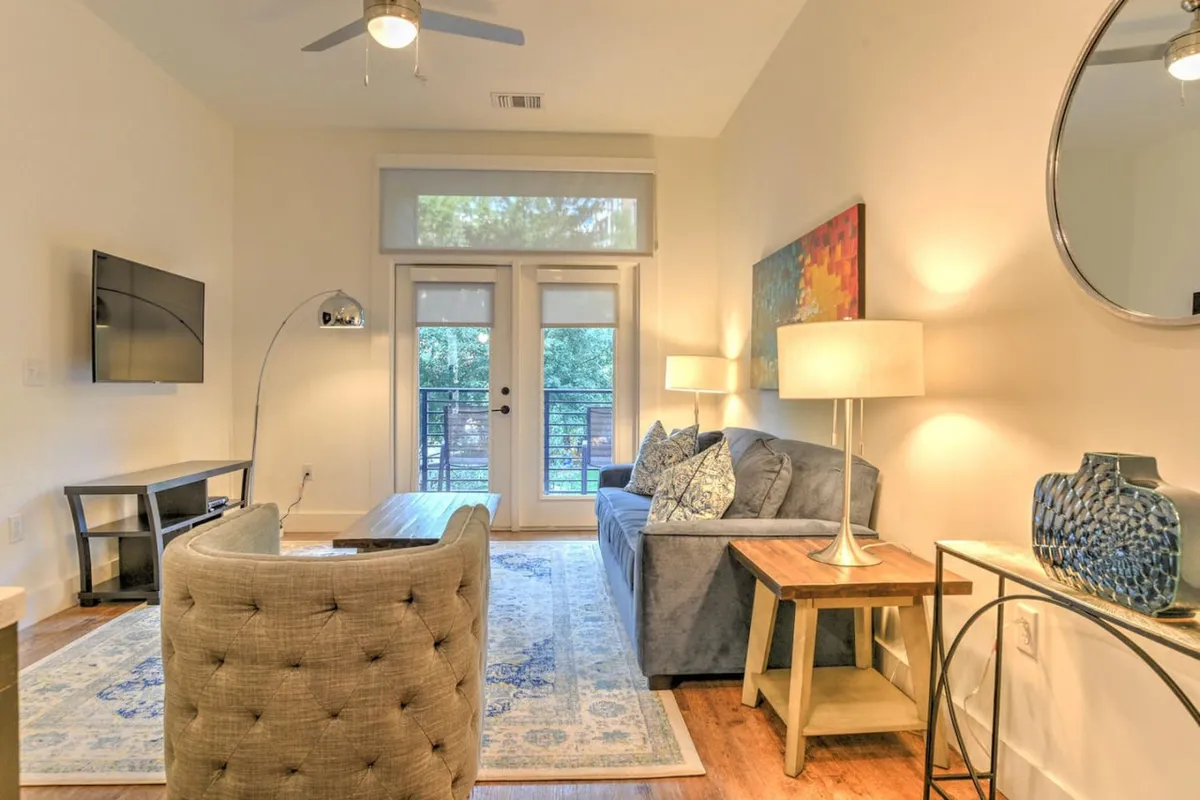 This image features a comfortable living room with a cozy sofa, a modern coffee table, eye-catching artwork on the wall, a floor lamp, and a television. The space is awash in natural light, offering an inviting atmosphere for relaxation, social gatherings, or quiet moments. The arrangement highlights both comfort and style, with thoughtful touches that reinforce the home's welcoming vibe.